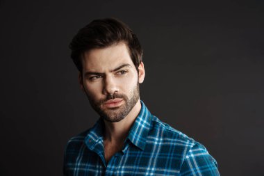 Tıraşsız yakışıklı adamın siyah arka planda yalnız poz verip bir kenara baktığını düşünmek.