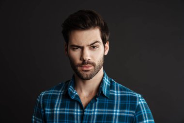 Tıraşsız yakışıklı adamın siyah arka planda yalnız poz verip kameraya baktığını düşünmek.