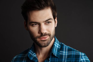 Tıraşsız yakışıklı adam siyah arka planda yalnız poz veriyor ve bir kenara bakıyor.