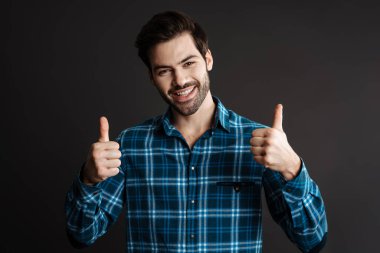 Gülümseyen ve parmaklarını gösteren neşeli yakışıklı adam siyah arka planda tek başına.