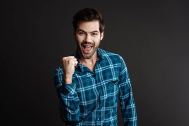 Heyecanlı yakışıklı adam çığlık atıyor ve kazanan jest yapıyor siyah arka planda izole edilmiş.