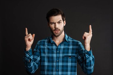 Kafası karışmış yakışıklı bir adam kameraya bakıyor ve gri arka planda yalnız bir şekilde parmağını yukarı kaldırıyor.