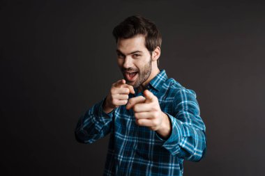 Heyecanlı yakışıklı esmer adam siyah arka planda izole edilmiş kamerayı işaret ediyor.