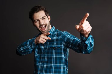 Heyecanlı yakışıklı esmer adam siyah arka planda izole edilmiş parmakları işaret ediyor.