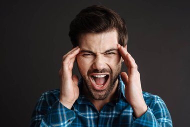 Mutsuz yakışıklı adam baş ağrısı içinde bağırıyor ve siyah arka planda tapınaklarını okşuyor.