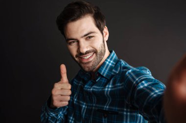 Siyah arka planda izole edilmiş selfie çekerken neşeli yakışıklı adam baş parmağını gösteriyor.
