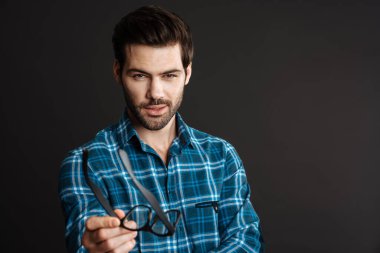 Siyah arka planda izole edilmiş kameraya gözlük uzatan kendine güvenen acımasız adam.