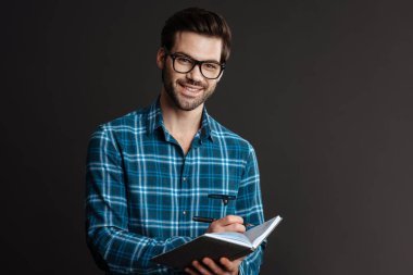 Gözlüklü gülen adam takvime siyah arka planda izole edilmiş notlar yazıyor.