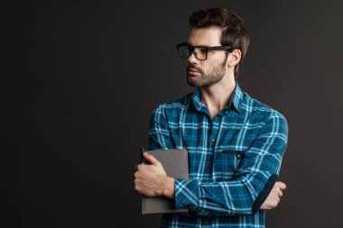 Gözlüklü, siyah arkaplanda izole edilmiş takvimle poz veren ciddi yakışıklı bir adam.