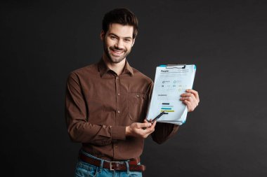 Gülümseyen ve diyagram gösteren neşeli yakışıklı iş adamı, siyah arka planda izole edilmiş.