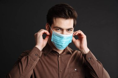 Siyah arka planda izole edilmiş koruyucu maske takan mutlu ve yakışıklı genç bir adam.