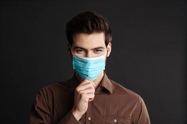 Siyah arka planda izole edilmiş koruyucu maske takan mutlu ve yakışıklı genç bir adam.