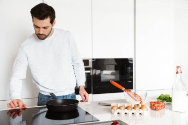 Ev mutfağında çırpılmış yumurta pişiren odaklanmış yakışıklı genç bir adam.