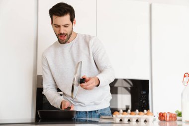 Mutfakta çırpılmış yumurta pişirirken kulaklık kullanan mutlu genç adam.