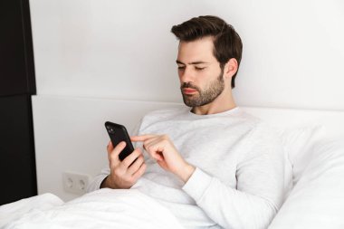 Evde dinlenirken cep telefonu kullanan yakışıklı bir adam.