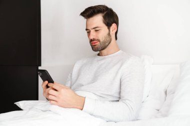 Evde dinlenirken cep telefonu kullanan yakışıklı bir adam.