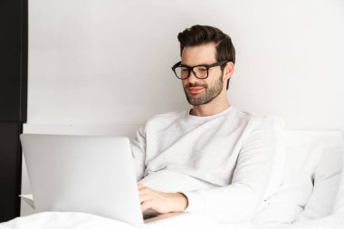 Gülümseyen genç adam evde dinlenirken dizüstü bilgisayar kullanıyor.