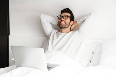 Gülümseyen genç adam evde dinlenirken dizüstü bilgisayar kullanıyor.