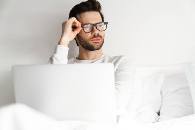 Evde yatarken dizüstü bilgisayar kullanan yakışıklı bir adam.