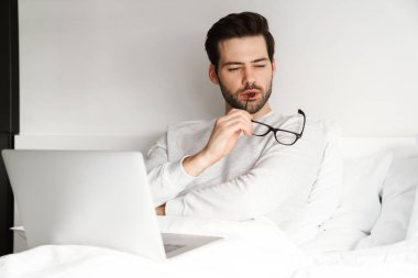 Evde yatarken dizüstü bilgisayar kullanan yakışıklı bir adam.