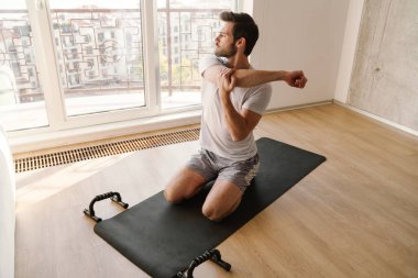 Odaklanmış atletik adam evde çalışırken kolunu esnetiyor.