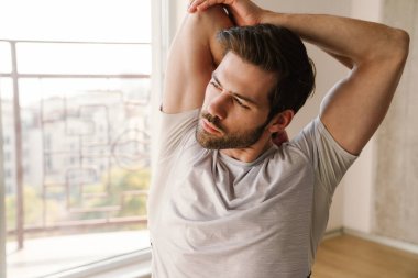 Odaklanmış atletik adam evde çalışırken kolunu esnetiyor.