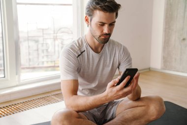 Ciddi atletik yakışıklı adam evde çalışırken cep telefonu kullanıyor.