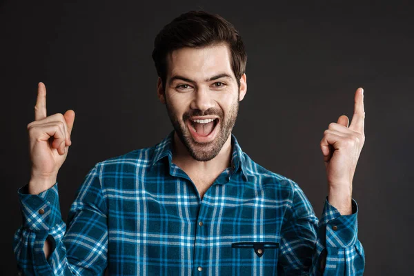 Excited handsome guy exclaiming and pointing finger upward isolated over black background