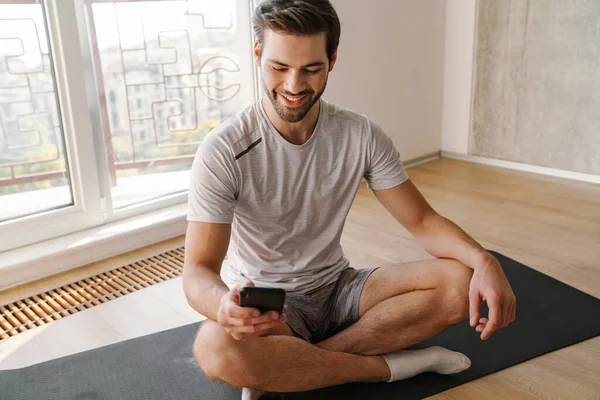 Happy athletic handsome man using mobile phone while working out at home