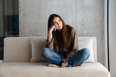 Mutlu esmer güzel kız evde kanepede otururken gülümsüyor.