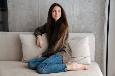 Mutlu esmer güzel kız evde kanepede otururken gülümsüyor.