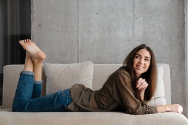 Evdeki kanepede yatarken gülümseyen güzel esmer kız.