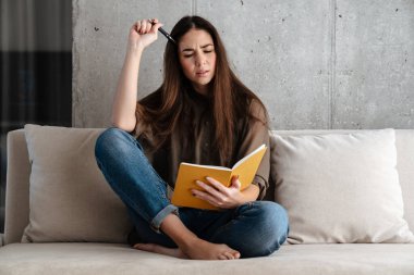 Düşünceli esmer güzel kız evdeki kanepede otururken notlar yazıyor.