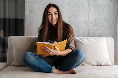 Mutlu esmer güzel kız evdeki kanepede otururken notlar yazıyor.