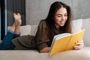 Mutlu esmer güzel kız evdeki kanepede yatarken notlar yazıyor.