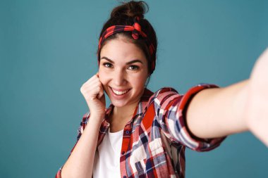 Mavi arka planda izole edilmiş selfie çekerken gülümseyen beyaz bir kadın.