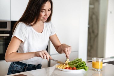 Ev mutfağında yemek yerken gülümseyen neşeli beyaz kadın.