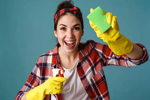 Joyful caucasian young woman in gloves cleaning glass isolated over blue background