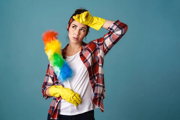 Exhausted young woman in gloves posing with colorful duster isolated over blue background