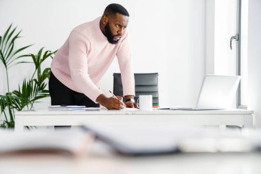 Ofiste çalışan kendine güvenen genç Afrikalı iş adamı, dizüstü bilgisayar kullanıyor.