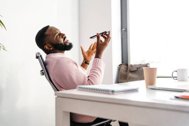 Ofis masasında otururken Afro-Amerikalı iş adamı cep telefonuyla konuşuyor.