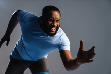 Gri arka planda tek başına koşan kendinden emin Afrikalı sporcu