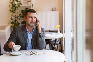 Kafedeki masada cep telefonuyla oturan kendine güvenen bir işadamı.