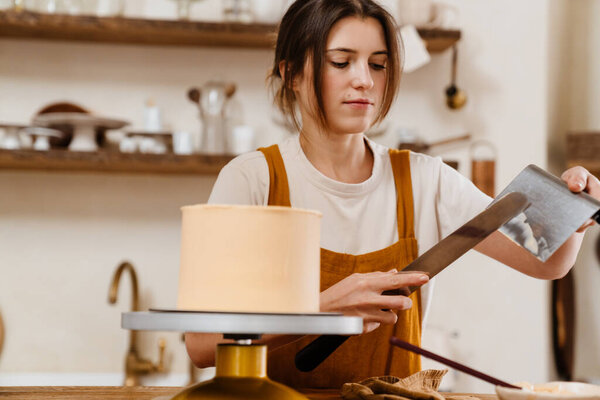 Beautiful concentrated pastry chef woman making cake with cream at cozy kitchen