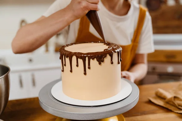 Caucasian pastry chef woman making cake with chocolate cream indoors