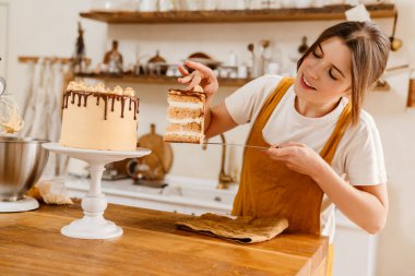Güzel, mutlu pasta şefi kadın sıcak mutfakta kremalı pasta gösteriyor.