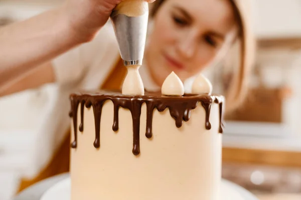 美しい焦点を当てたペストリーシェフの女性は居心地の良いキッチンでチョコレートクリームとケーキを作る — ストック写真