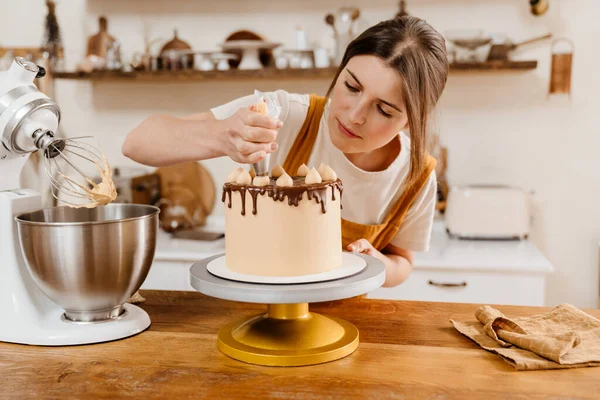 美しい焦点を当てたペストリーシェフの女性は居心地の良いキッチンでクリームとケーキを作る — ストック写真