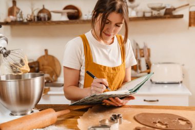 Mutfakta Noel kurabiyesi pişirirken not yazan memnun pasta şefi kadın.