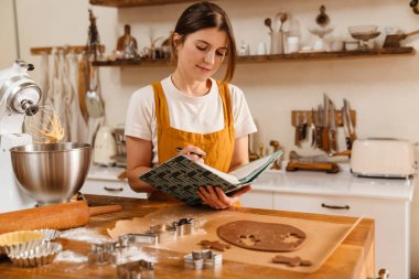 Mutfakta Noel kurabiyesi pişirirken not yazan memnun pasta şefi kadın.